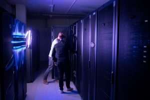 Zwei Mitarbeiter arbeiten an Serverschrank in unserem Rechenzentrum mit blauer Beleuchtung