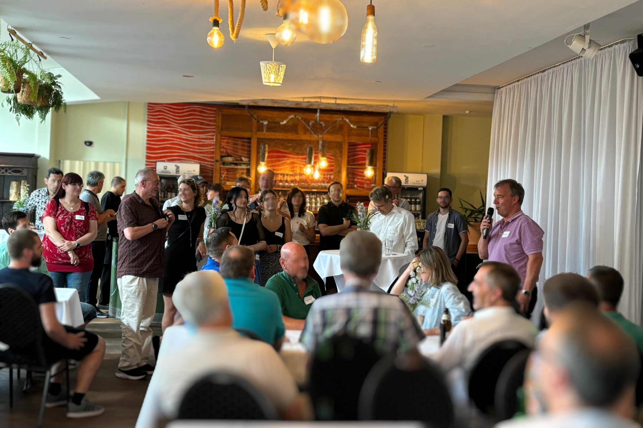 Eine größere Gruppe von Mitarbeitenden auf der Feier, die der Rede von dem Geschäftsführer zuhören